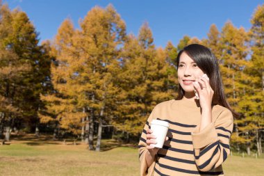 Kadın konuşmak için cep telefonu ve kahve ormanında tutarak