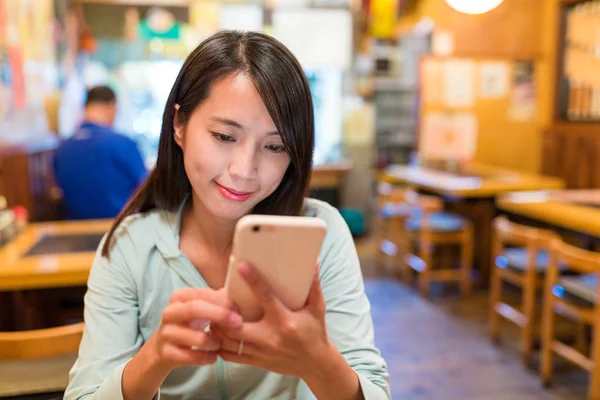 Женщина смотрит на мобильный телефон в ресторане — стоковое фото