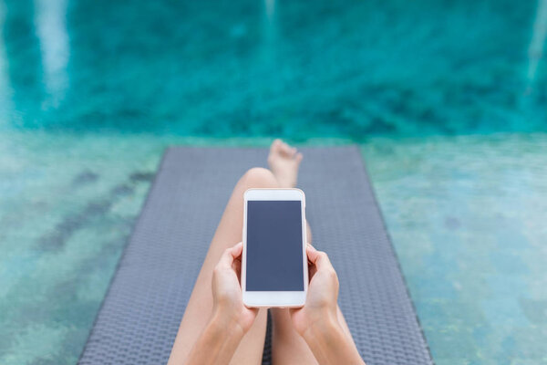 Woman working on mobile phone at poolside 