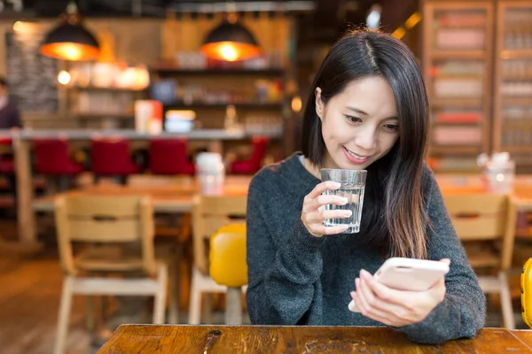 Жінка дивиться на мобільний телефон і пити склянку води — стокове фото