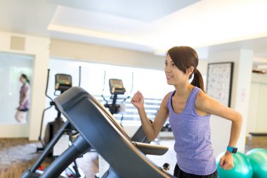 Spor salonunda bir koşu bandı içinde çalışan kadın 