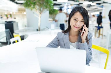 Kullanarak dizüstü bilgisayar ve cep telefonu üzerinde konuşurken bir işkadını