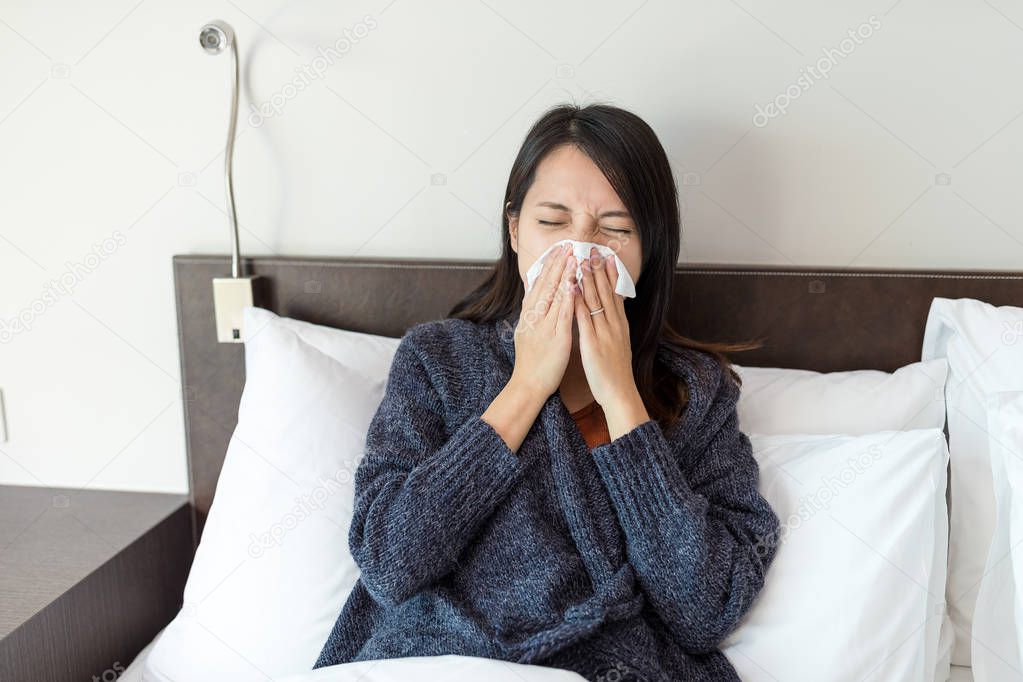 Woman sneezing on bed