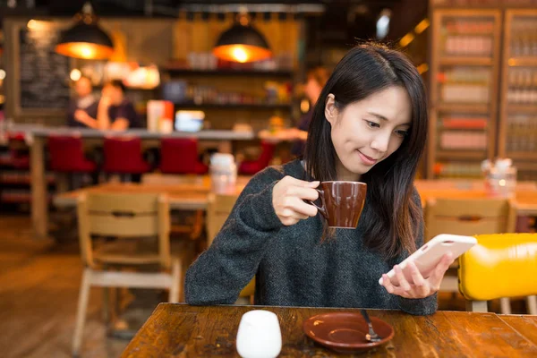 Женщина пьет кофе и пользуется мобильным телефоном — стоковое фото