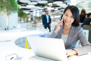 Telefonda konuşmak ve dizüstü bilgisayar üzerinde çalışan kadın