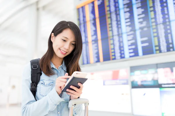 Женщина, проверяющая рейс по мобильному телефону с расписанием в задней части — стоковое фото
