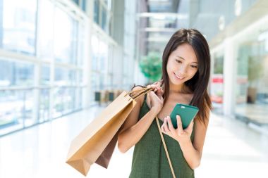 Alışveriş torbaları tutarak ve cep telefonu kullanan kadın