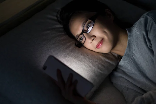 Nő keres a mobiltelefon ágyon — Stock Fotó