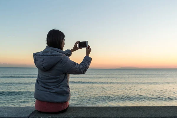 Mulher tirando foto com paisagem marinha e pôr do sol — Fotografia de Stock