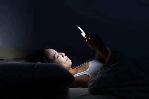 Mulher usando celular e deitado na cama — Fotografia de Stock