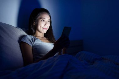 Yatak üstünde hareket eden telefon üzerinde çalışan kadın