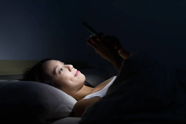 Wanita menggunakan ponsel dan berbaring di tempat tidur — Stok Foto