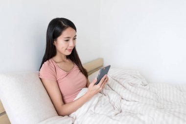 Yatakta akıllı telefon kullanan kadın.