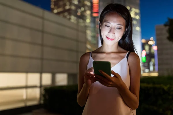 Mujer mirando por celular en la ciudad por la noche — Foto de Stock