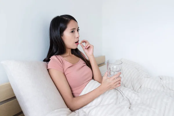 Frau nimmt Tabletten und sitzt auf Bett — Stockfoto