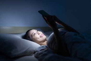 Geceleri yatakta cep telefonu kullanan kadın