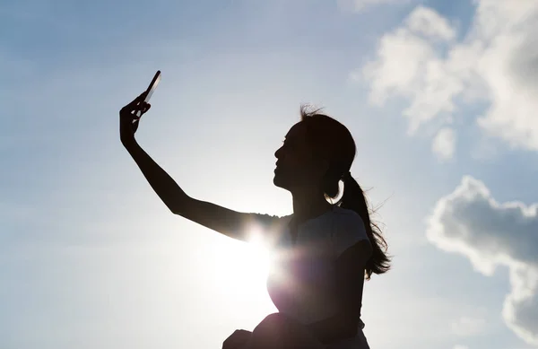 Woman taking selfie with mobile phone under sunset — Stock Photo, Image