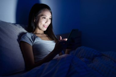 Geceleri yatakta cep telefonu kullanan kadın