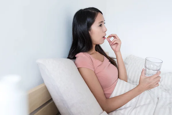 Mujer tomando pastillas y acostada en la cama —  Fotos de Stock