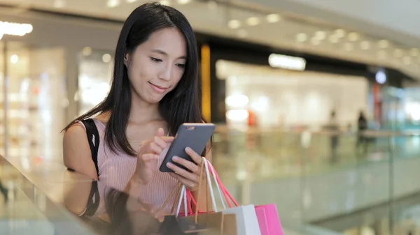 Mulher usando smartphone e segurando sacos de compras — Fotografia de Stock
