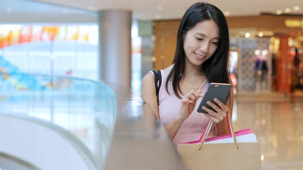 Frau benutzt Smartphone und hält Einkaufstüten in der Hand — Stockfoto