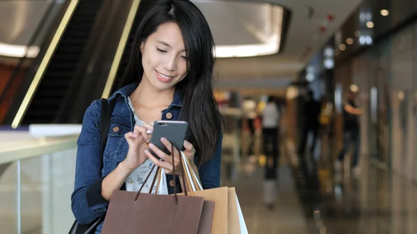 Vrouw met behulp van de mobiele telefoon en houden van boodschappentassen — Stockfoto