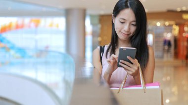 Cep telefonu kullaranarak ve kağıt torba taşıyan kadın