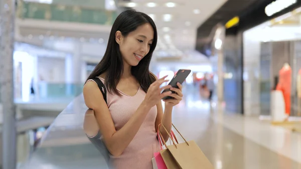 Vrouw met behulp van de mobiele telefoon en houden van boodschappentassen — Stockfoto