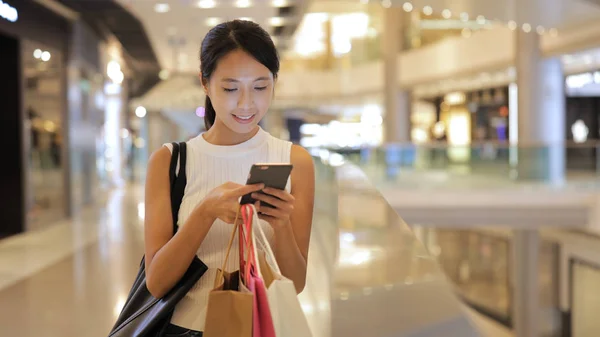 Nő keresi a mobiltelefon és a gazdaság bevásárló táskák — Stock Fotó