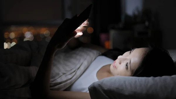 Frau schaut aufs Smartphone und liegt im Bett — Stockfoto