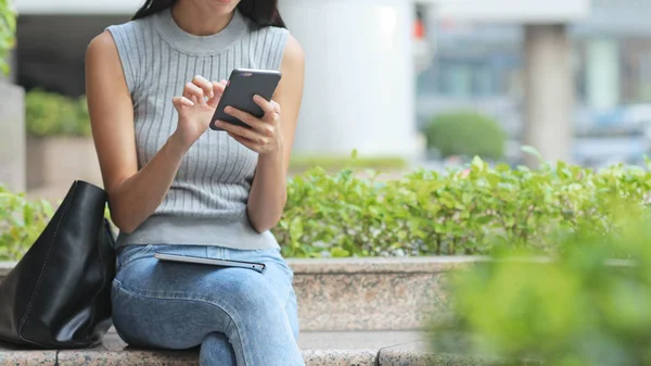 Mujer usando el teléfono celular y sentada al aire libre —  Fotos de Stock