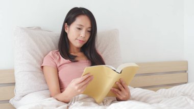 Kadın yatakta kitap okuyor. 