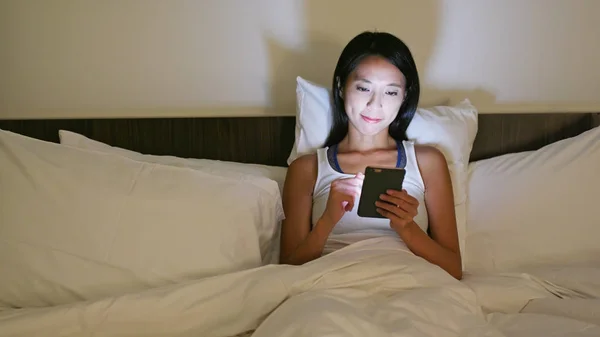 Vrouw met behulp van smartphone en liggend op bed — Stockfoto