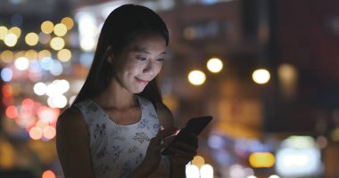 Gece şehirde akıllı telefon kullanan bir kadın. 