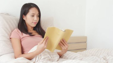 Kadın yatakta kitap okuyor. 