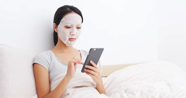 Vrouw toepassen gezichtsmasker en zittend op bed — Stockfoto