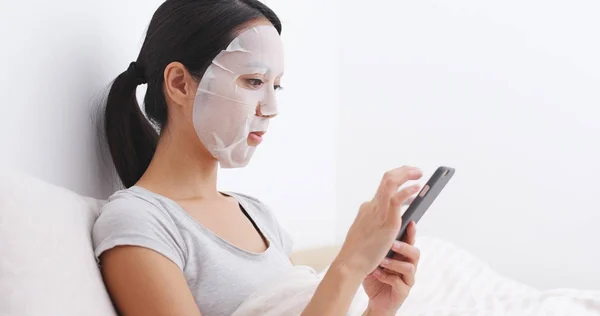 Perempuan menerapkan masker wajah dan menggunakan ponsel — Stok Foto