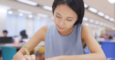 Ödevini Üniversitesi kampüsü kitaplığındaki üzerinde çalışan kadın 