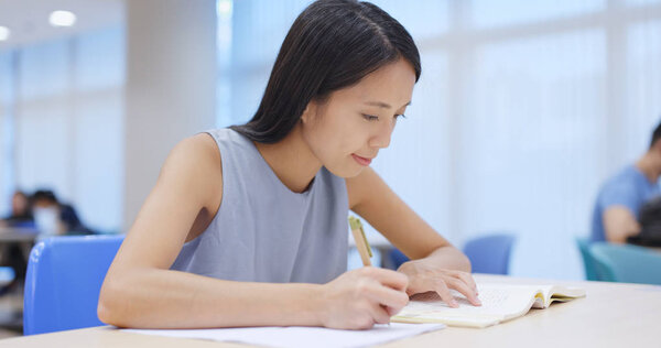 Woman writing on her homework in library 