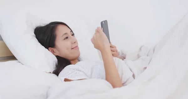 Woman using cellphone and lying on bed — Stock Photo, Image