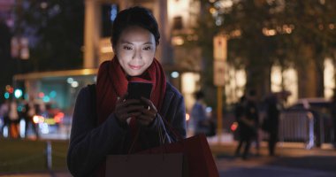 Gece şehirde akıllı telefon kullanan bir kadın.