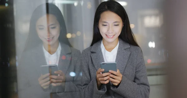 Businesswoman using mobile phone with window reflection