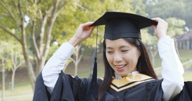 Mezuniyet giyen kadın cüppe ve kolej parkta düzeltmek 