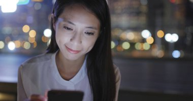 Gece şehirde akıllı telefon kullanan bir kadın. 