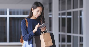 Cep telefonu kullaranarak ve alışveriş torbaları tutan kadın 