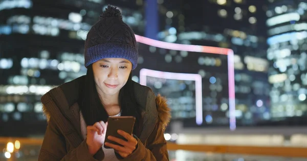 Woman wearing winter knit hat and jacket with using smart phone over beautiful cityscape background at night