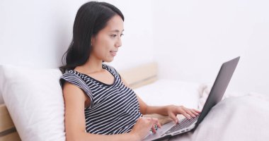 Dizüstü bilgisayarda çalışarak ve yatağın üstüne oturan kadın