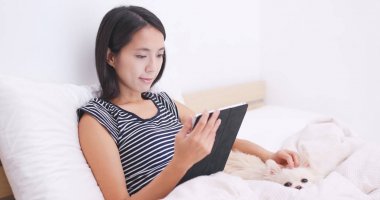 Dijital tablet üzerinde izliyor ve köpeğiyle yatakta yatarken kadın 