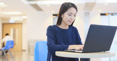 Üniversite kampüsü içinde dizüstü bilgisayar üzerinde çalışan öğrenci