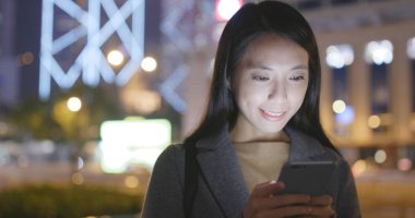 Gece şehirde akıllı telefon kullanan bir kadın. 